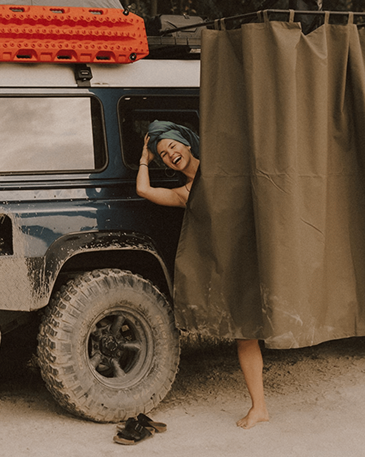 Off‑road vehicle with a roof rack and side‑mounted shower or privacy enclosure in an outdoor setting.