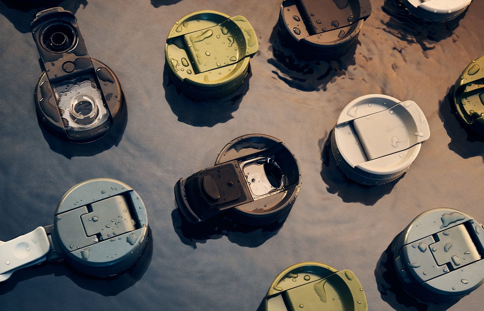 Assorted insulated drinkware lids with water droplets floating in shallow outdoor water.
