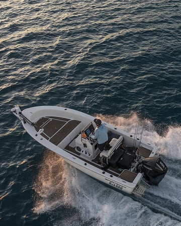 Two people on a boat at sunset with an open green Dometic cool box on the deck containing drinks.